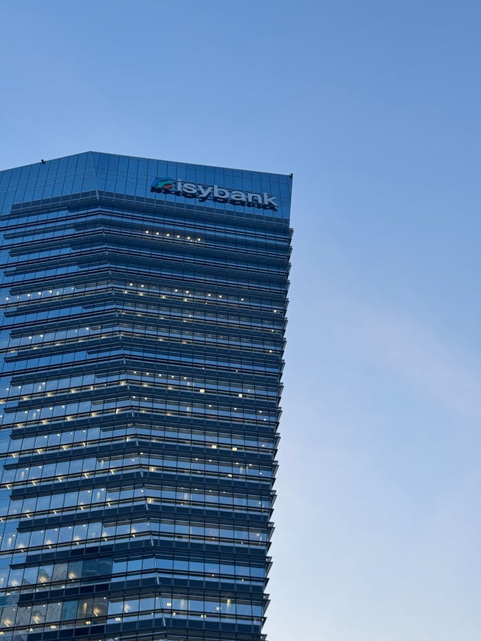 A tall glass skyscraper in Milan with Isybank logo against a clear blue sky.